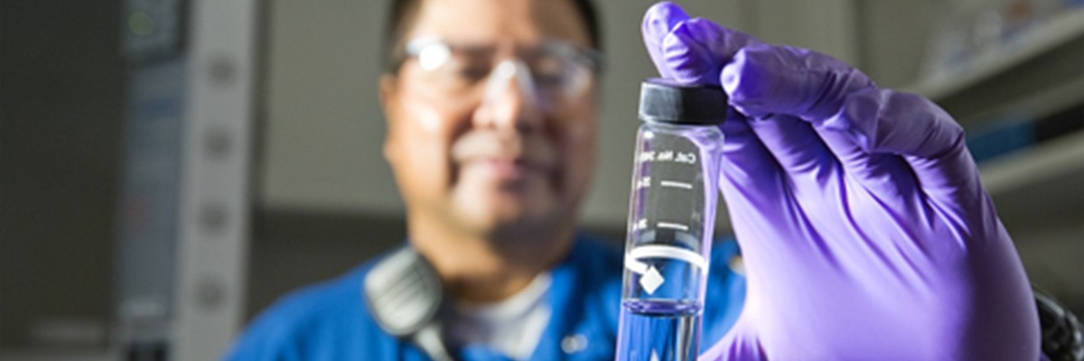 Man in lab looking at glass vial